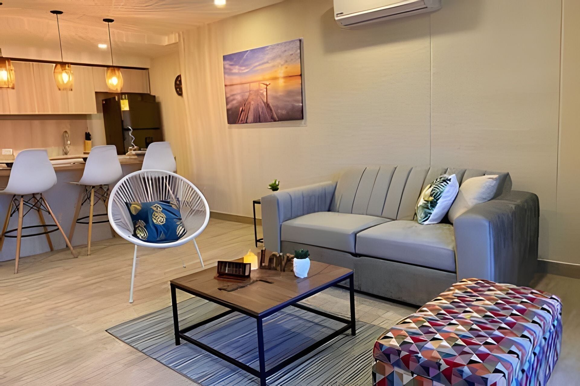 A modern living room with a sofa, a coffee table, a patterned ottoman, and a chair with a cushion.