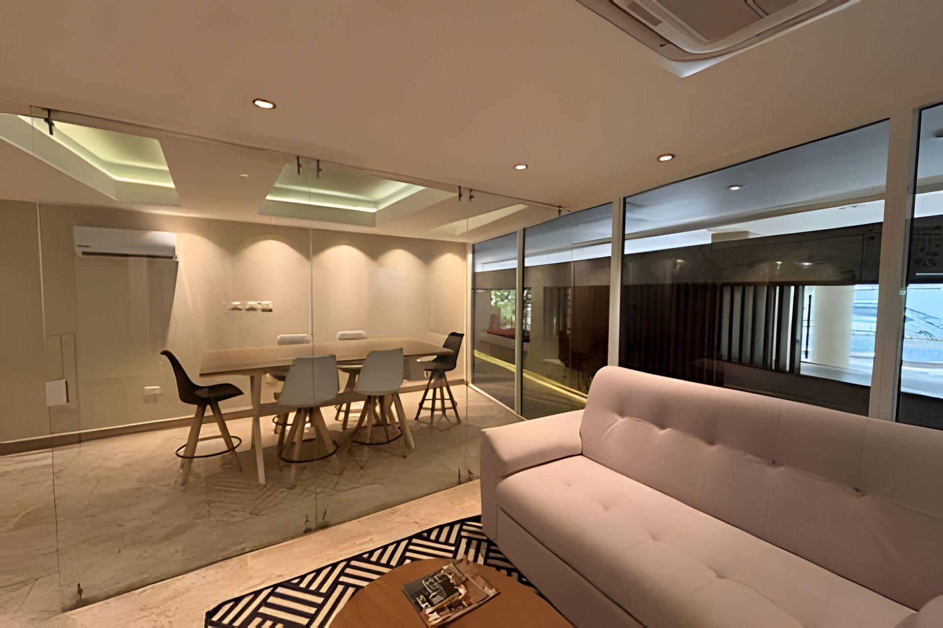 A modern living room with a sofa, a dining area with chairs, a coffee table, and large windows.