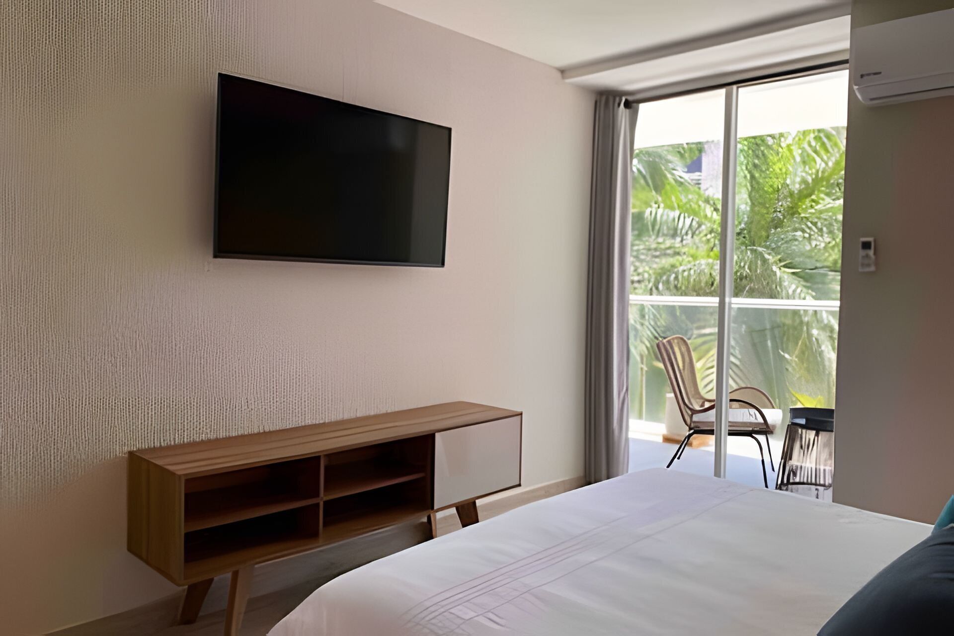 Ein modernes Hotelzimmer mit einem großen Bett, einem an der Wand befestigten Fernseher, einem Holzkonsolentisch und einem Balkon mit Stühlen.