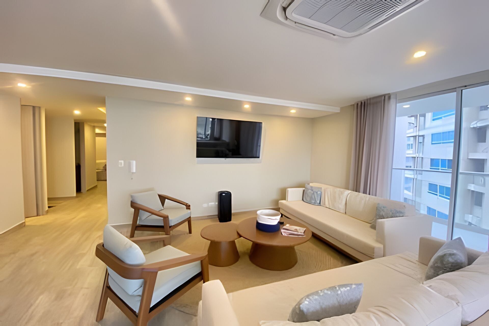 A modern living room with a sofa, armchairs, a coffee table, and a flat-screen TV mounted on the wall.