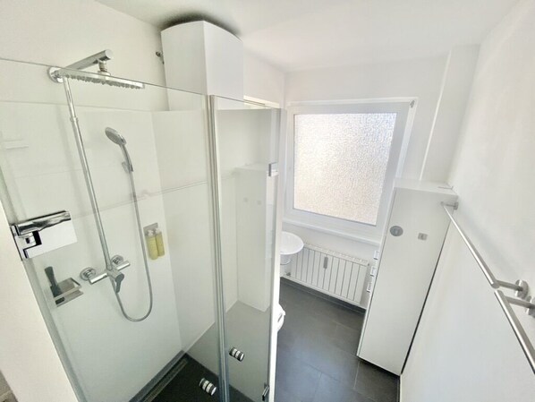 A modern bathroom with a glass shower enclosure, a white sink, and a window providing natural light.