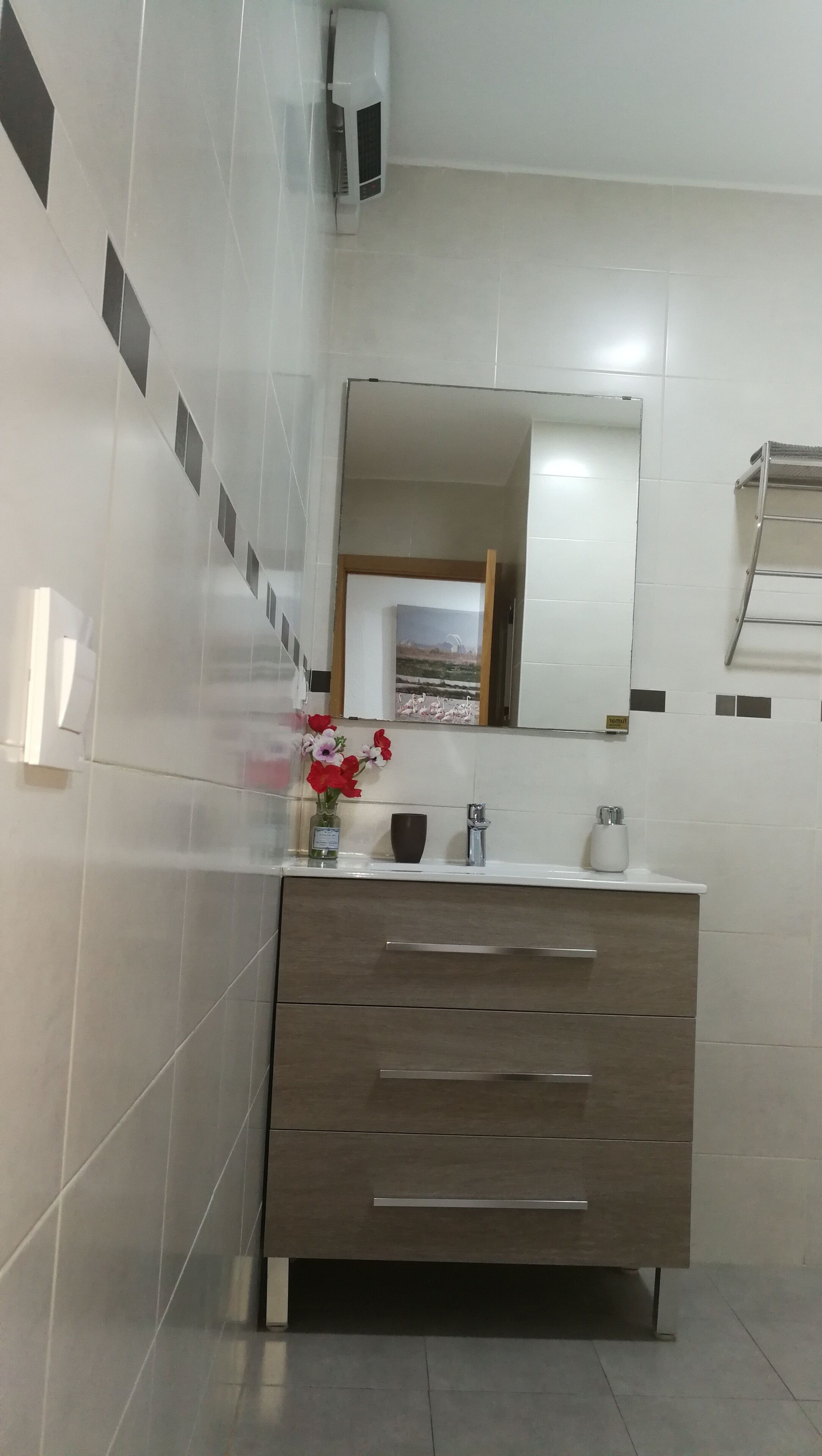 Un baño moderno con un espejo grande, un tocador con cajones, un perchero y un florero con flores.