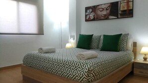 Een net opgemaakt bed met beddengoed met dessin, twee kussens en twee opgerolde handdoeken.