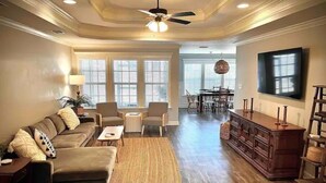 A spacious living room with a sofa, chairs, a coffee table, a wooden cabinet, and a television. - Cozy Cottage in Convenient Hahira Location (Hahira)