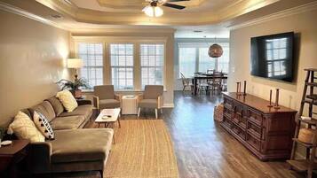 A spacious living room with a sofa, chairs, a coffee table, a wooden cabinet, and a television.