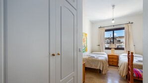 A bedroom with two beds, a window with curtains, a bedside lamp, and a painting on the wall. - Marina Duquesa 2411 Sea View Penthouse (Manilva)