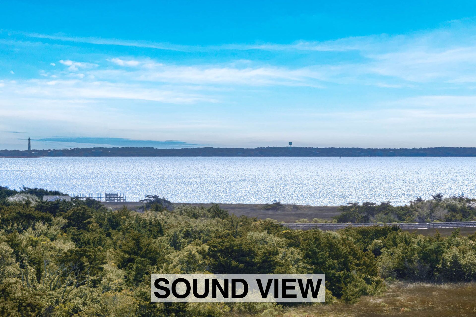 Une vue pittoresque d’une étendue d’eau, avec un phare à l’horizon et une forêt dense au premier plan.