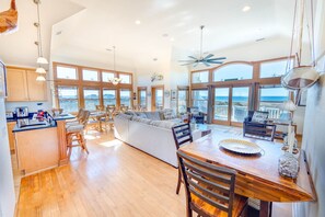 A spacious kitchen with wooden cabinets, a dining area with a wooden table and chairs, and large windows offering ocean views. - Soundside Avon Home with Private Pool, Hot tub, Game Room and Theater Room (Avon)