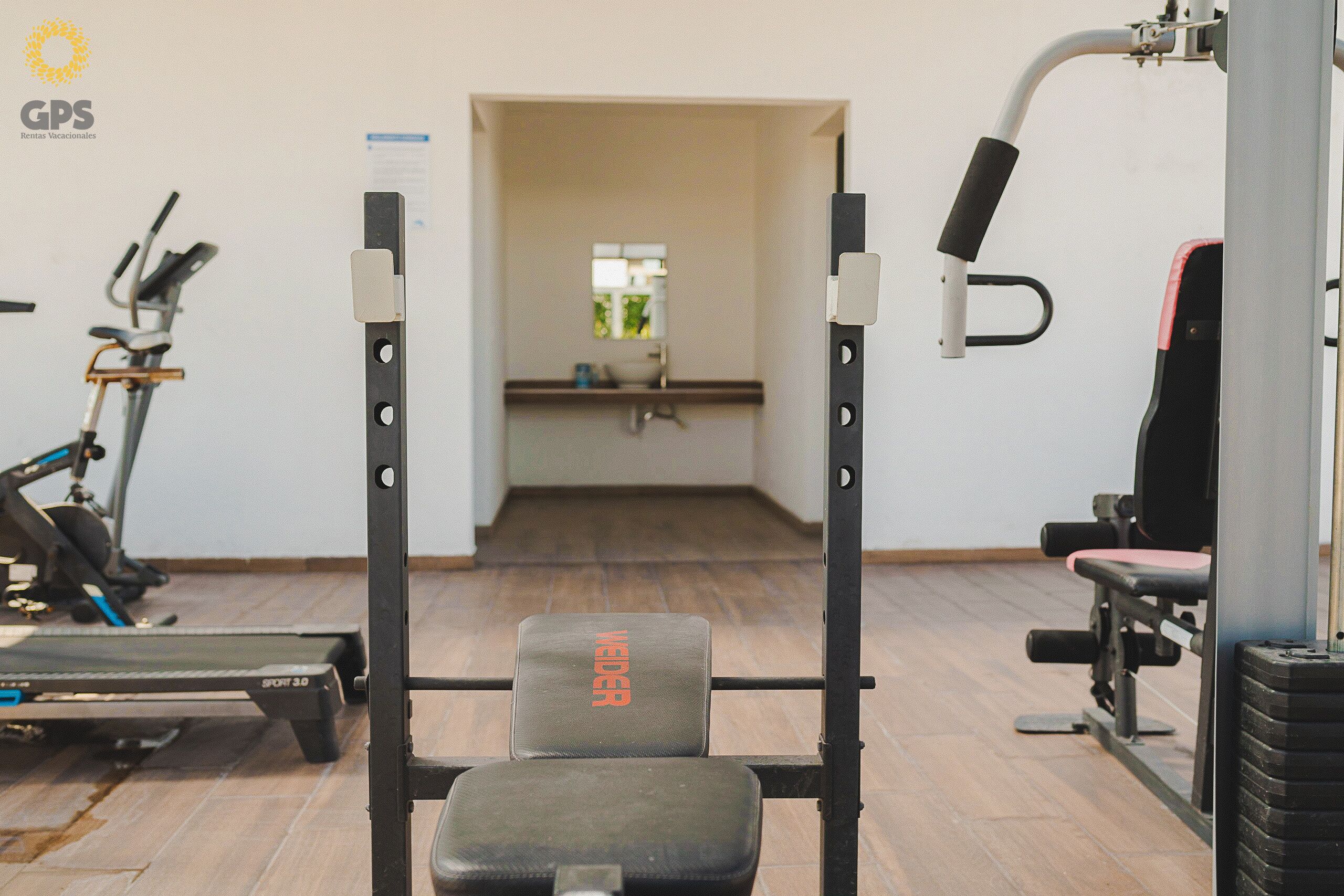 A gym with a weight bench, exercise equipment, and a window in the background.