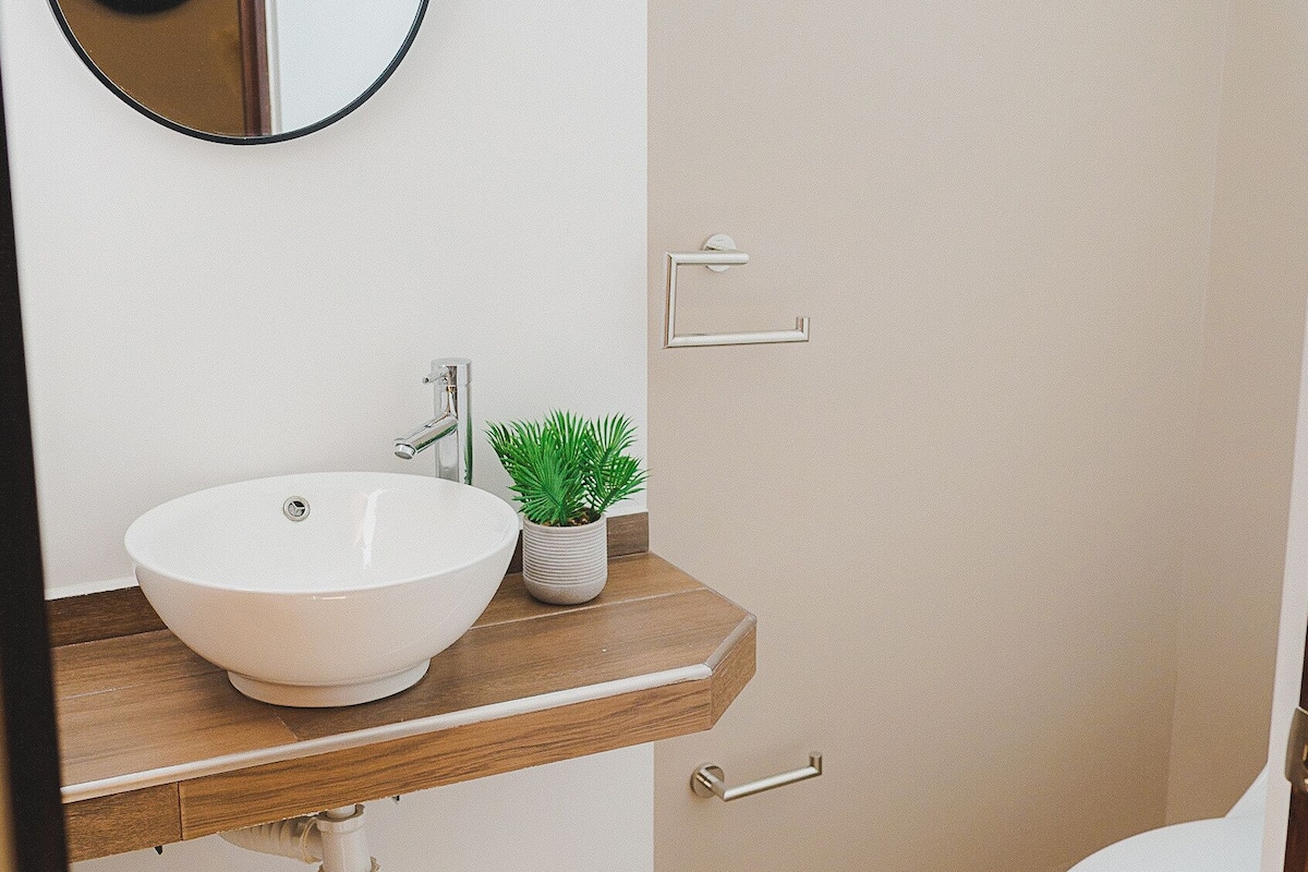 A bathroom with a white sink, a round mirror, a small potted plant, and a toilet.