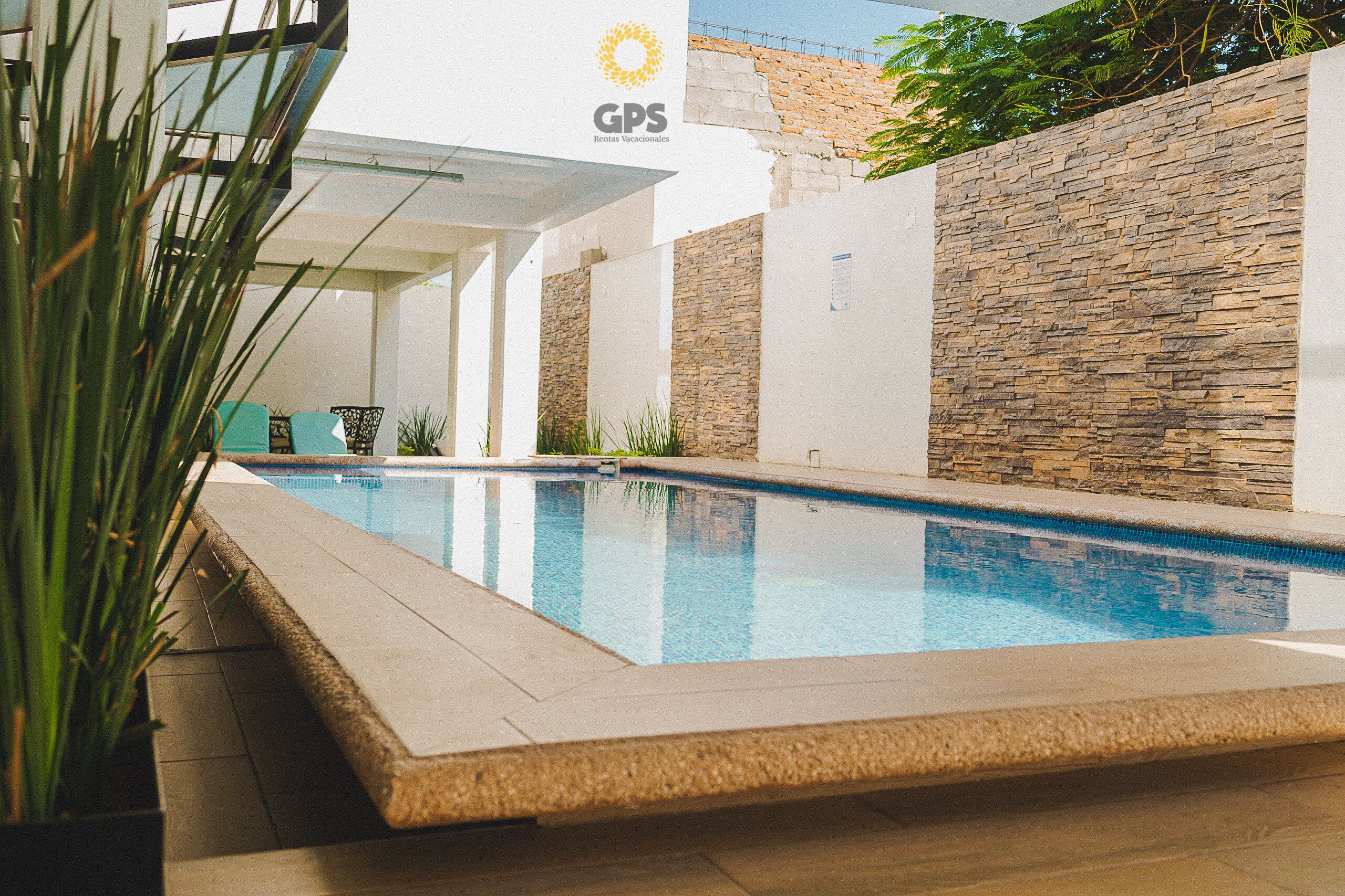 A swimming pool with a stone wall and a sign for GPS Rentals Vacacionales.