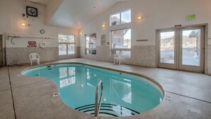 An indoor swimming pool with clear water, a lifeguard chair, and a sign indicating shallow water. - Newly Updated 5 Bedroom Townhome with Gorgeous Deck Views! (Silverthorne)
