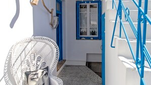 Ein weißes Gebäude mit blauen Akzenten, eine Treppe mit blauen Geländern und ein weißer Korbstuhl mit blauer Sitzkissen.
