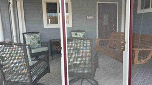 Eine überdachte Veranda mit Korbstühlen, einer Bank, einem kleinen Tisch und einem Deckenventilator.