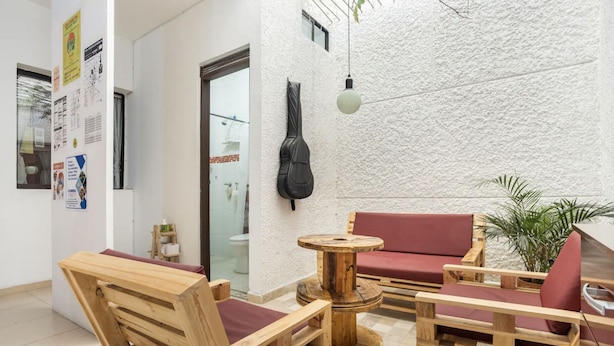 A wooden furniture arrangement with a red sofa and chairs, a small round table, and a hanging guitar. - Casa Clandestina (MedellÃn)