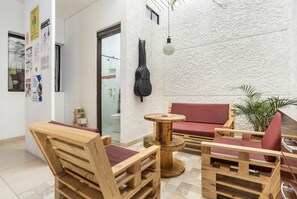 A wooden furniture arrangement with a red sofa and chairs, a small round table, and a hanging guitar. - Casa Clandestina (Medellín)