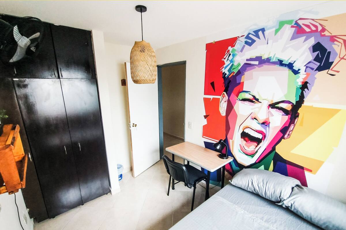 Quarto com uma cama, uma escrivaninha, uma cadeira, um guarda-roupa e um mural colorido na parede.