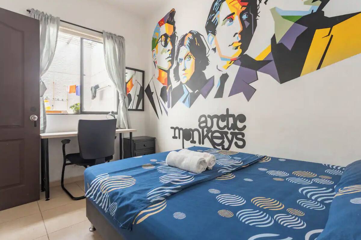 Quarto de hotel com cama, escrivaninha e janela com cortinas.