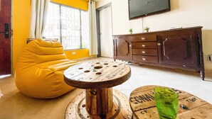A living room with a yellow bean bag chair, a round wooden coffee table, and a television mounted on the wall. - Casa Clandestina (MedellÃn)
