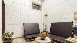 A cozy outdoor seating area with two dark-colored sofas and a small round table, surrounded by potted plants and a checkered floor. - Casa Clandestina (MedellÃn)
