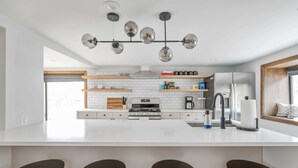 Eine moderne Küche mit einer zentralen Kochinsel, Barhocker, einem Edelstahlkühlschrank und einer hängenden Leuchte.