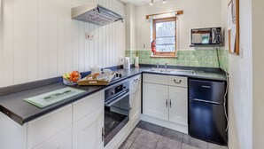 Une cuisine moderne avec des meubles blancs, un réfrigérateur noir, un four à micro-ondes et une fenêtre donnant sur une maison.
