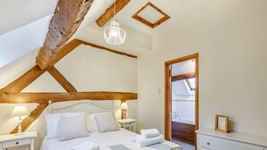 Une chambre avec un grand lit, des tables de chevet avec des lampes, une poutre en bois au plafond et une vue sur la salle de bain par une porte ouverte.