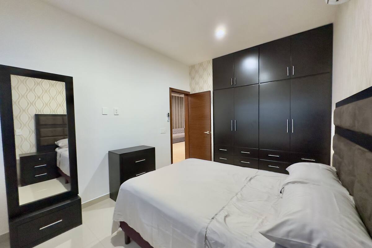 Un dormitorio con cama, armario, cómoda y espejo.