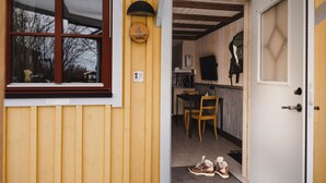A wooden building with a window, a door, and a small kitchen area with a table and chairs. - Epokgården (Öregrund)
