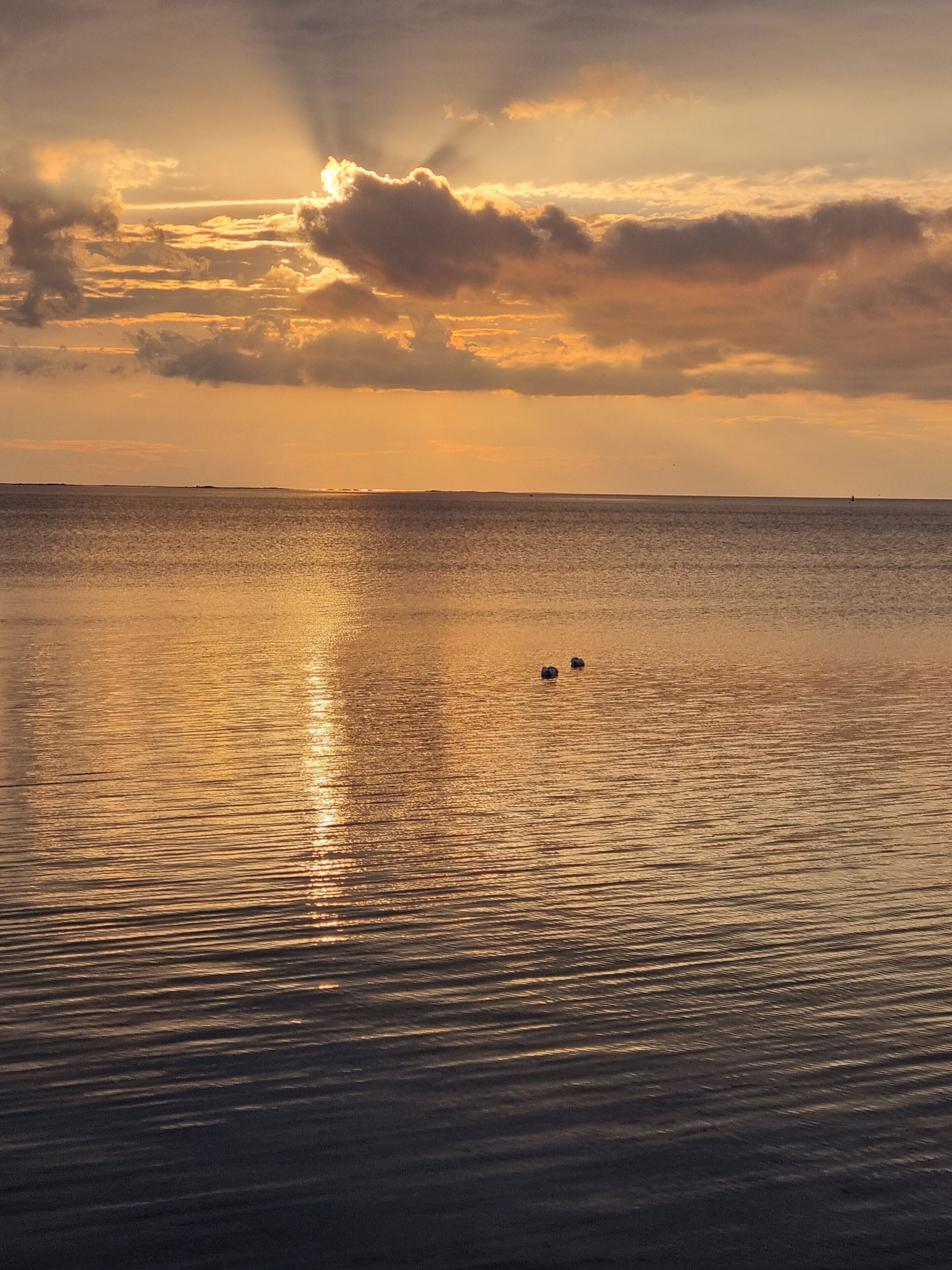 A calm sea at sunset with two boats in the distance.
