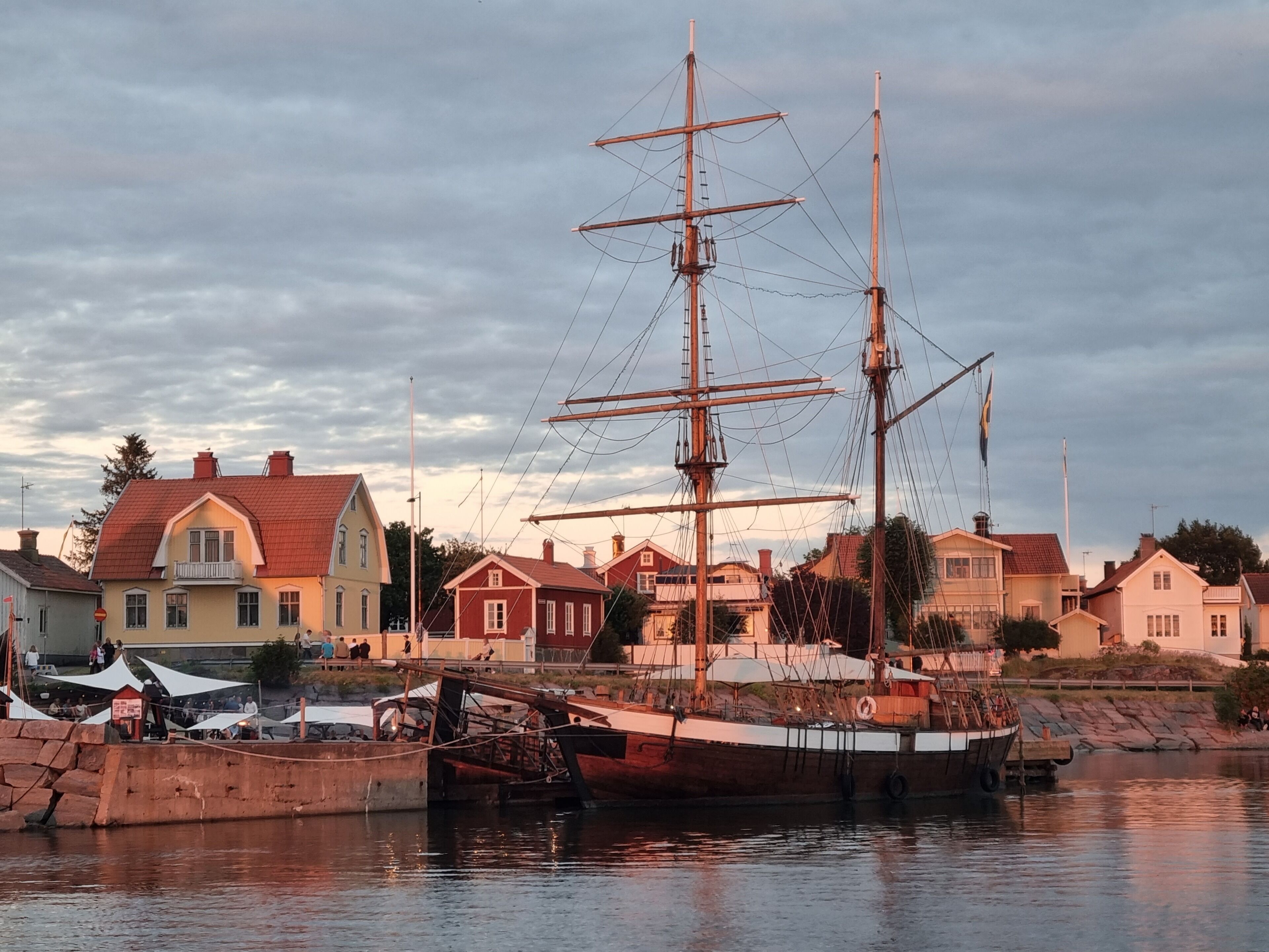 A historic sailing ship docked at a harbor with residential buildings in the background.
