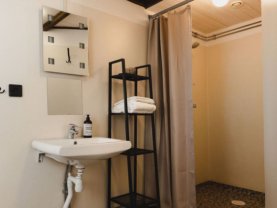 Un baño con lavamanos, espejo, reloj, toallero y cortina de ducha.