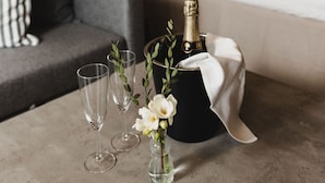 A room with a bed, a grey sofa, a small table with glasses and flowers, and a bottle of champagne. - Epokgården (Öregrund)