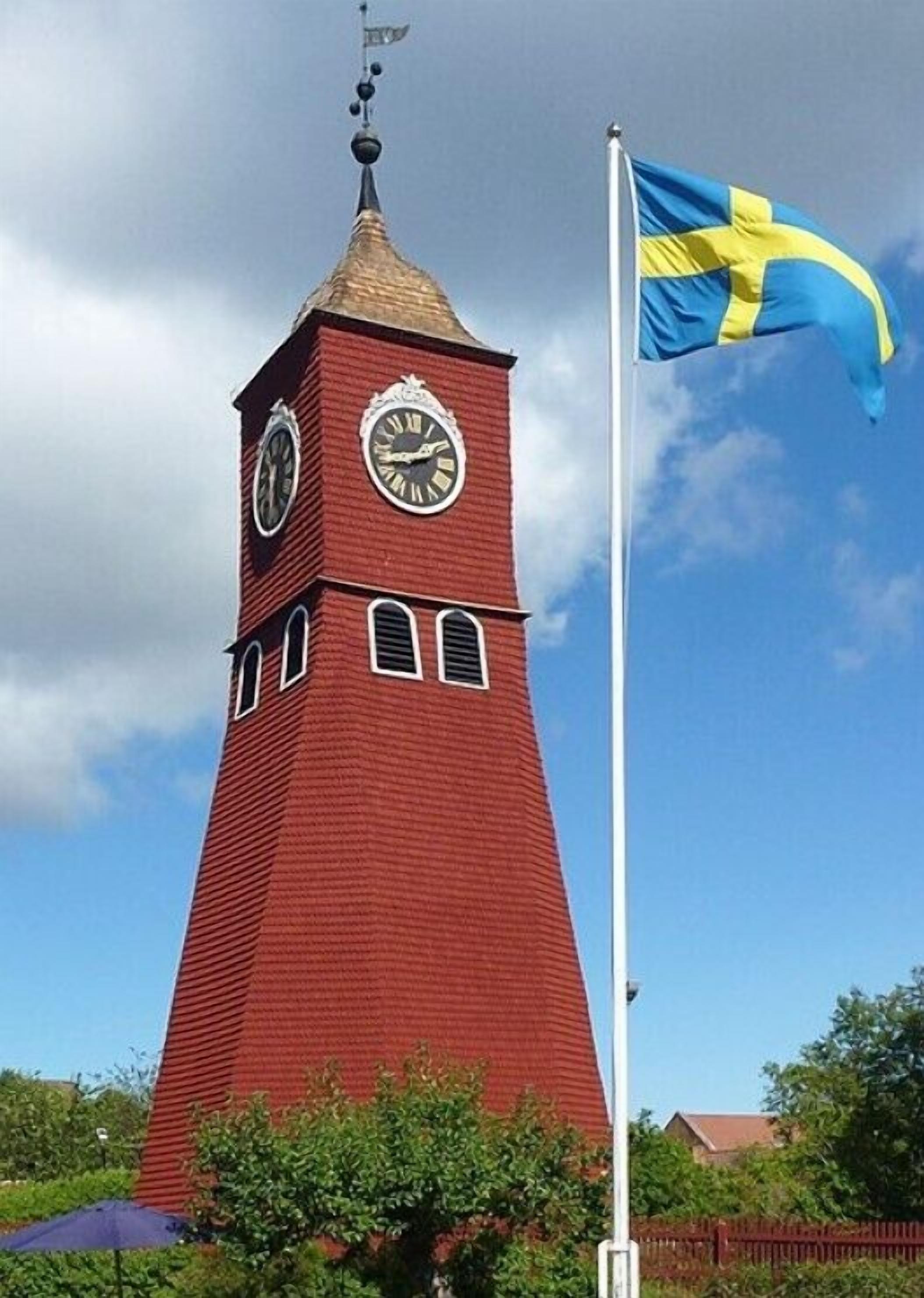 A red clock tower with a flagpole and a flag.