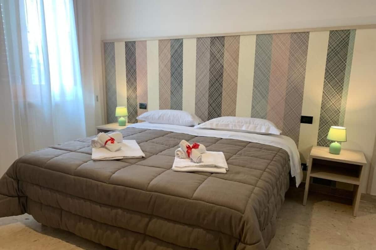 A hotel room with a large bed, two bedside tables with lamps, and a headboard with a striped pattern.