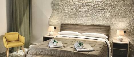 A bedroom with a bed, a wooden bench, a yellow chair, and a stone wall.