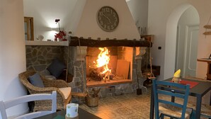 A cozy living room with a stone fireplace, a clock on the wall, wicker furniture, and a table with a candle. - Villa Anna (Brindisi)