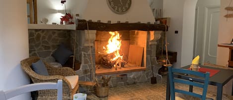 A cozy living room with a stone fireplace, a clock on the wall, wicker furniture, and a table with a candle.