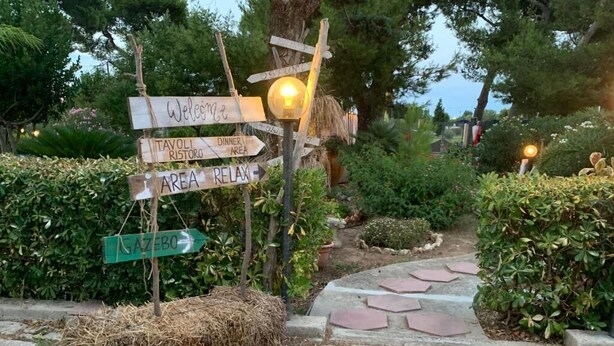 A rustic outdoor area with stone pathways, wooden signs, and a hay bale. - Villa Anna (Brindisi)