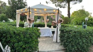 A gazebo with a table set up for an event, surrounded by greenery and stone pathways. - Villa Anna (Brindisi)