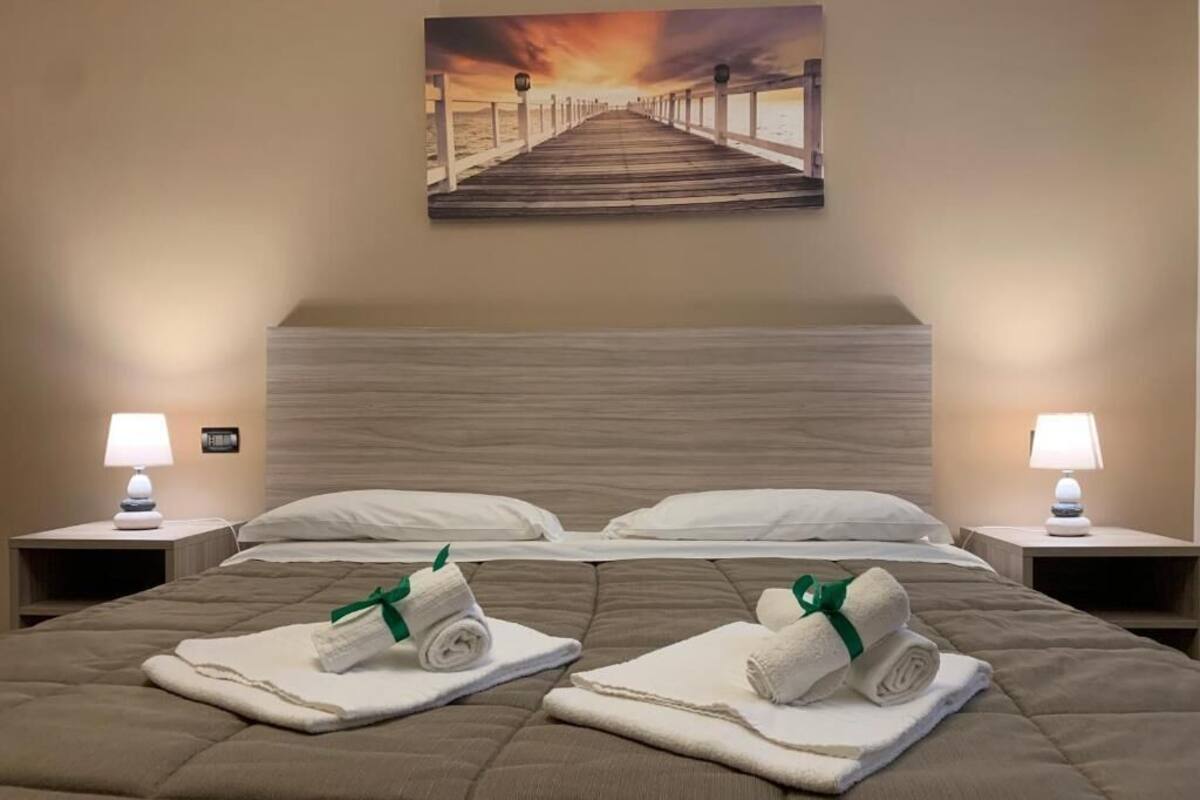 A hotel room with a large bed, two nightstands, a painting of a pier, and towels on the bed.