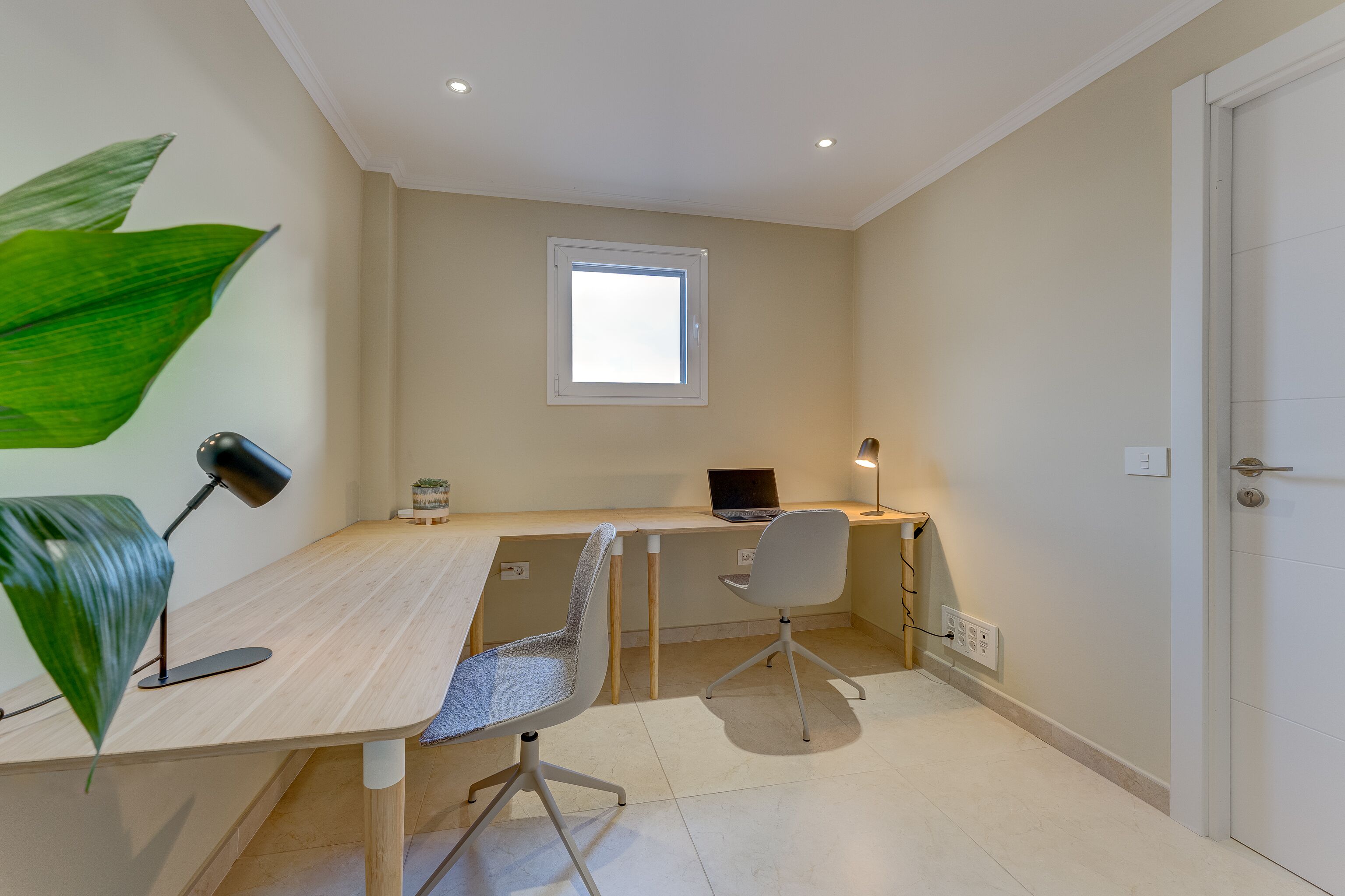 Un espace de bureau moderne comprenant un bureau, deux chaises, un ordinateur portable et une fenêtre.