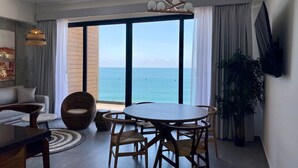 A modern living room with a large window, a dining table, and a sofa. - Catania Apartments (Mazatlán)