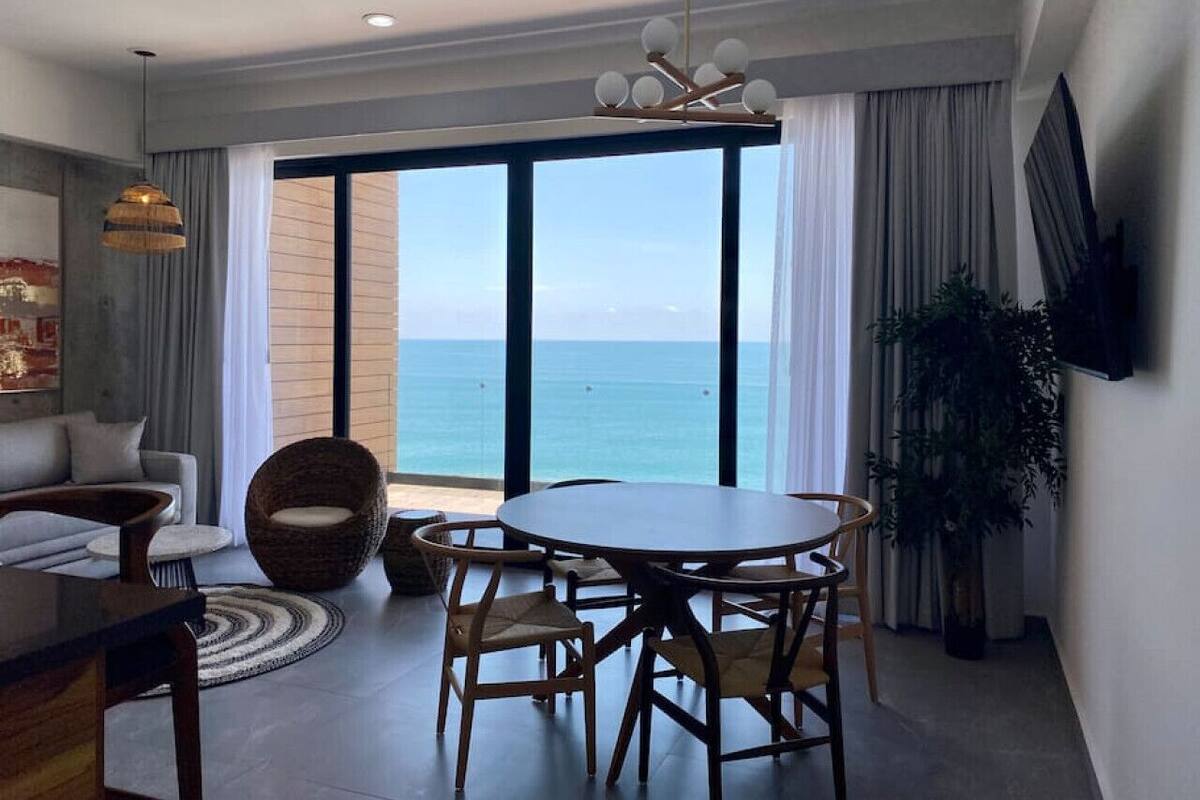A modern living room with a large window, a dining table, and a sofa.