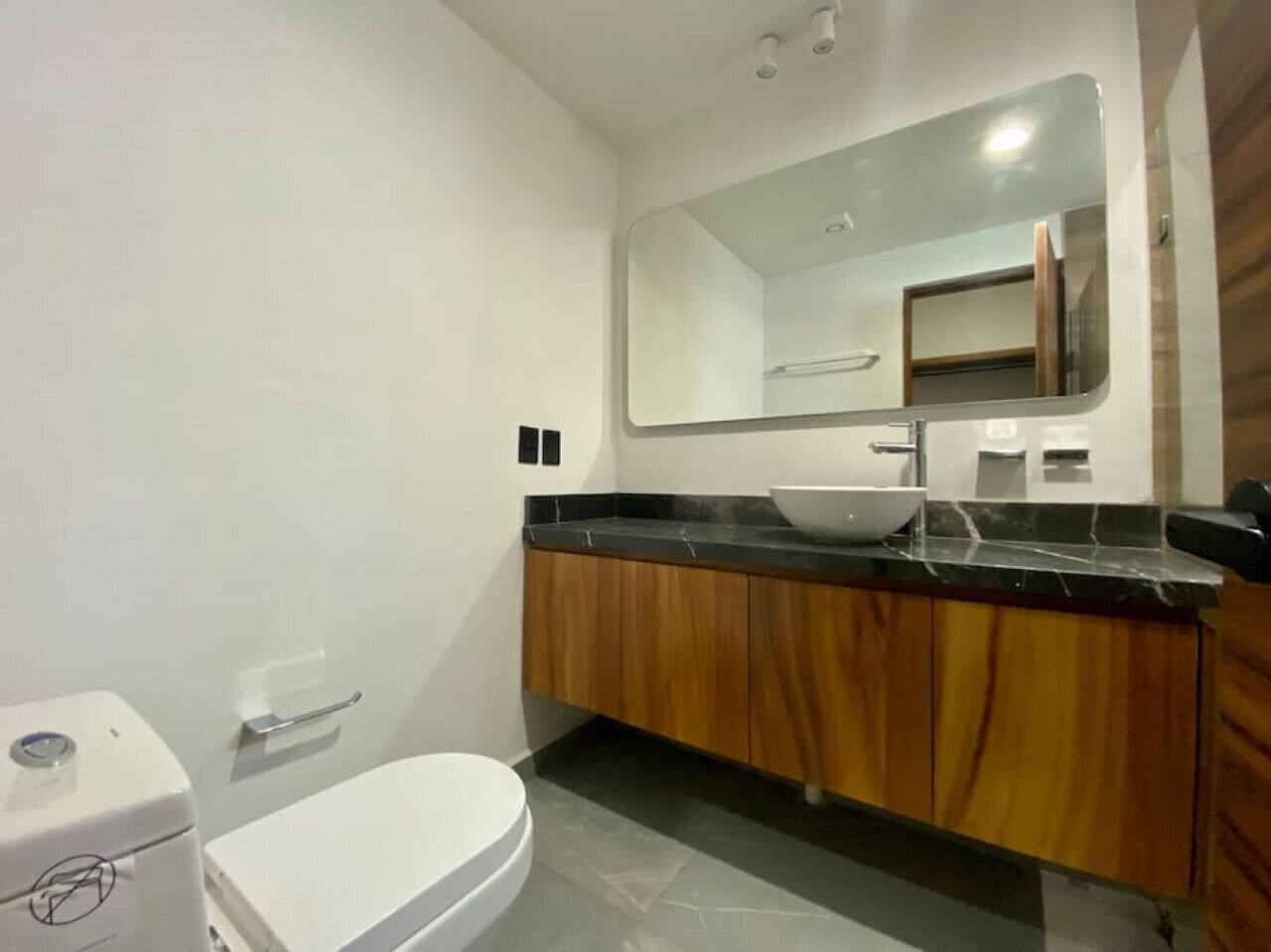A modern bathroom with a white toilet, a sink with a black countertop, and wooden cabinets.