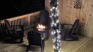 A deck with a fire pit, two Adirondack chairs, and a decorative tree wrapped with lights. - Sugarbush Mountain Home (Sky Valley)