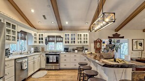 A spacious kitchen with wooden floors, white cabinetry, and a central island with stools. - Sugarbush Mountain Home (Sky Valley)