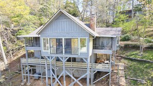 A two-story wooden house with a balcony on the upper floor, surrounded by trees and a stone pathway. - Sugarbush Mountain Home (Sky Valley)