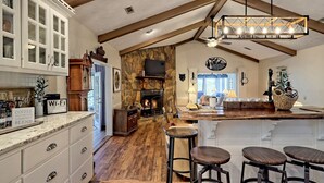 A kitchen with a stone fireplace, wooden beams, and a bar area with stools. - Sugarbush Mountain Home (Sky Valley)
