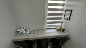 A dining area with a table, chairs, a welcome sign, a framed certificate, and a window with blinds.